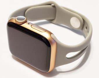 May include: A rose gold Apple Watch with a grey silicone sport band. The band has two cutouts on the side.