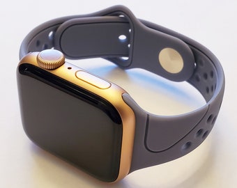 May include: A gold Apple Watch with a grey silicone sport band. The band has a textured design and a small hole pattern.