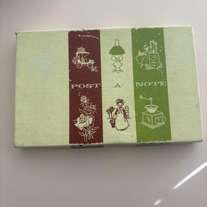 May include: A rectangular box with a light green background and three vertical panels in burgundy and green. The panels feature illustrations of a carriage, a lamp, and a woman. The words "POST A NOTE" are printed on the box.