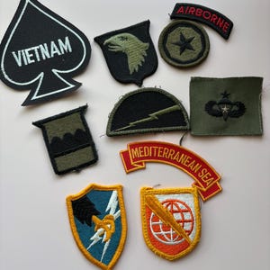 May include: A collection of embroidered military patches in various shapes and colors. Includes a black spade with "VIETNAM" in white, an eagle, a star, and a patch with "AIRBORNE". Other patches feature lightning bolts, a globe, and "MEDITERRANEAN SEA".