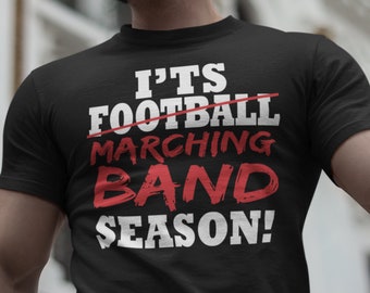 Puede incluir: Camiseta negra con texto blanco que dice "It's Football Marching Band Season!" con la palabra "Football" tachada y la palabra "Marching" en rojo.