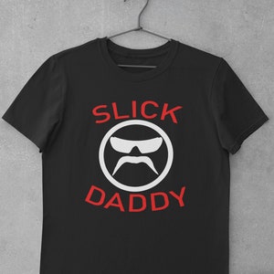 Könnte beinhalten: Schwarzes T-Shirt mit einem weißen Kreis-Motiv, das ein stilisiertes Gesicht mit Sonnenbrille und Schnurrbart zeigt. Der Text "SLICK DADDY" ist in Rot über und unter dem Kreis.
