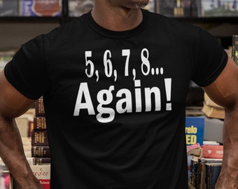 Puede incluir: Una camiseta negra con el texto "5, 6, 7, 8... Again!" en blanco. La persona de la imagen lleva gafas de sol y está de pie en una habitación llena de libros e instrumentos musicales.