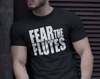 Może przedstawiać: Czarny T-shirt z białym napisem "FEAR THE FLUTES". Osoba w tym T-shircie stoi obok ceglanego muru.