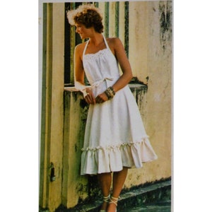 May include: A white halter dress with a lace-trimmed bodice and a flared skirt. The dress features a tie waist and a ruffled hem. The model is wearing a bracelet and sandals. The dress is a vintage style.