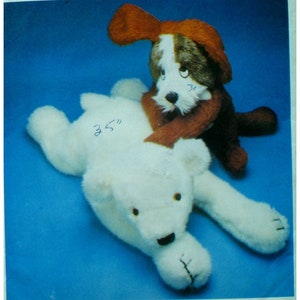 Puede incluir: Un oso polar de peluche blanco acostado con un perro de peluche marrón y blanco sentado encima. El oso polar mide 3,5 pulgadas de largo.