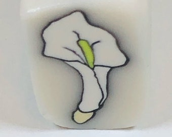May include: A white flower with a green center, drawn on a white ceramic tile.