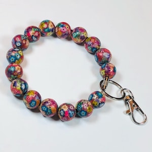 May include: A colorful beaded bracelet with a floral pattern and a silver key chain attached.