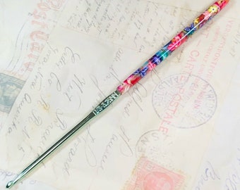 May include: A close-up of a colorful crochet hook with a floral design. The hook is made of metal and has a green handle. The hook is labeled "SIZE 3.5 MM".