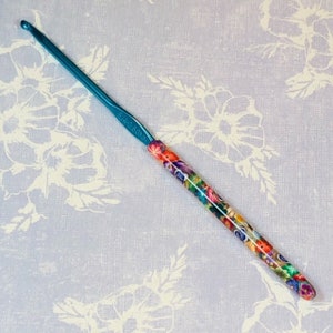 May include: A teal crochet hook with a colorful floral pattern on the handle.
