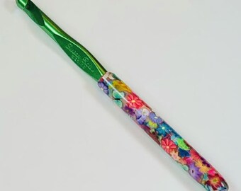 May include: A green crochet hook with a colorful floral pattern on the handle. The hook is made by Susan Bates.