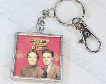 May include: A silver keychain with a red and white framed image of a couple. The image has the text "we've been through a lot".