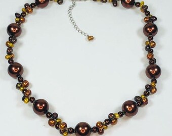 May include: A brown and gold pearl necklace with a silver clasp. The necklace is made of large, round pearls and smaller, round beads.