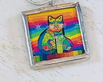 May include: A silver chain necklace with a square pendant featuring a colorful illustration of two cats on a rainbow background.