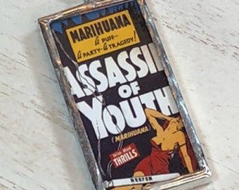 May include: A silver framed glass pendant with a vintage comic book cover image. The cover features a woman in a red dress and the text "Marihuana - A Puff - A Party - A Tragedy! Assassin of Youth (Marihuana) - With Hot Thrills - Number 1".
