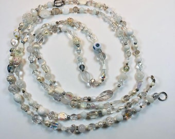 May include: A long, layered necklace featuring a variety of beads in shades of white, clear, and iridescent. The beads include pearls, crystals, and decorative elements. The necklace is designed to be worn long and has a silver-tone clasp.