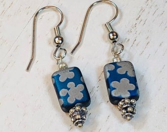 May include: A pair of silver dangle earrings with blue and silver floral patterned beads. The beads are rectangular and have a silver bead at the bottom.