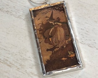 May include: A rectangular pendant with a silver-colored frame. The pendant features a sepia-toned illustration of a witch in a pointed hat, holding a lantern, with a black cat. The background shows trees and birds.