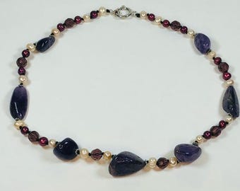 May include: A purple and cream necklace with a silver clasp. The necklace is made of small beads and features larger, irregularly shaped purple stones.