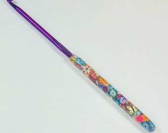 May include: A purple crochet hook with a colorful floral design on the handle.