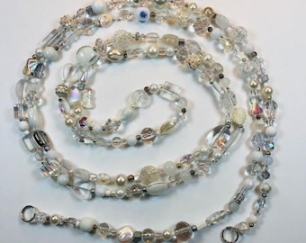 May include: A long, layered necklace featuring a variety of beads in shades of white, clear, and iridescent. The beads include pearls, faceted crystals, and opaque white beads. The necklace is arranged in a spiral pattern, with a clasp at the end.