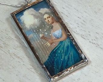 May include: A silver pendant necklace with a rectangular glass charm featuring a painting of a woman in a blue dress standing under a cloud with rain falling.