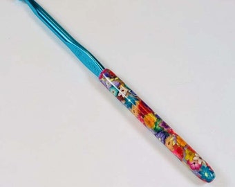 May include: A turquoise crochet hook with a colorful floral pattern on the handle. The hook is labeled "11/8 (3.5mm)".
