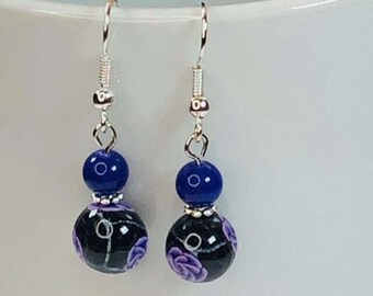 May include: A pair of dangle earrings with a black and white floral design and a dark blue bead. The earrings have silver hooks.