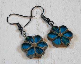 May include: A pair of earrings with blue and green flower-shaped charms hanging from black metal hooks.
