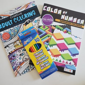 May include: Two adult coloring books with a pack of 10 colored pencils. The book on the left is titled "Creative Adult Coloring" and features a colorful design. The book on the right is titled "Color by Number Advanced Coloring" and features a geometric design. The pack of pencils is yellow with black text and features the words "Colored Pencils, Crayons de couleur, L&aacute;pices de Color".
