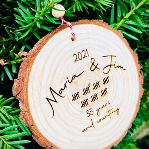 May include: A wooden ornament with the text "2021 Maria & Jim" and "35 years and counting" with hash marks representing the years.
