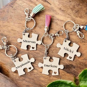 K&ouml;nnte beinhalten: F&uuml;nf Schl&uuml;sselanh&auml;nger in Form von Puzzleteilen mit verschiedenen Namen auf jedem Teil: Sharon, Stephanie, Darlene, Nicki und ein f&uuml;nftes Teil ohne Namen. Jeder Schl&uuml;sselanh&auml;nger hat einen kleinen Quasten in einer anderen Farbe: dunkelrot, gr&uuml;n, rosa, blau.