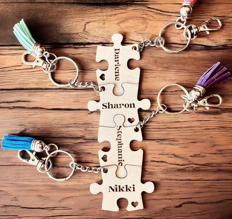 K&ouml;nnte beinhalten: Vier Holzschachtelteile mit den Namen Darlene, Sharon, Stephanie und Nikki eingraviert. Jedes Teil hat eine kleine Herzform ausgeschnitten und ist durch eine silberne Kette und einen Ring mit dem n&auml;chsten Teil verbunden. Die Teile sind an Schl&uuml;sselringen mit blauen, violetten und gr&uuml;nen Quasten befestigt.