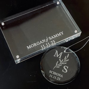 May include: A clear acrylic frame with the text "MORGAN & SAMMY 11.11.23" engraved on it. A clear glass ornament with the text "M & S SCIBONA 11.11.23" engraved on it.