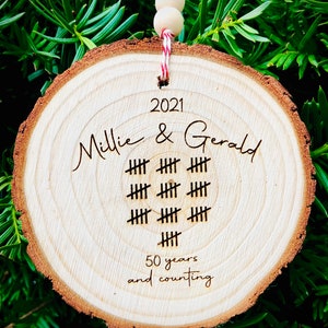 May include: A wooden round ornament with the text "2021 Millie & Gerald" and a tally mark design representing 50 years. The text "50 years and counting" is also included.