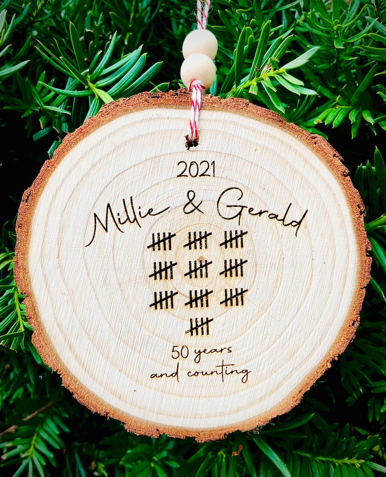 May include: A wooden round ornament with the text "2021 Millie & Gerald" and a tally mark design representing 50 years. The text "50 years and counting" is also included.