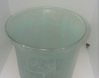 Op de afbeelding: Een gematteerde glazen kom met een lichtblauwe tint, rustend op een basis van kleine schelpen.