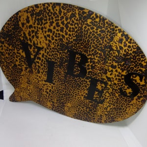 May include: A brown and black leopard print speech bubble with the word "VIBES" in black letters.