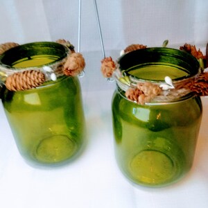 Peut inclure: Deux bougeoirs en verre vert avec des poignées en fil de fer et une garniture rustique en ficelle brune et blanche et en pommes de pin.