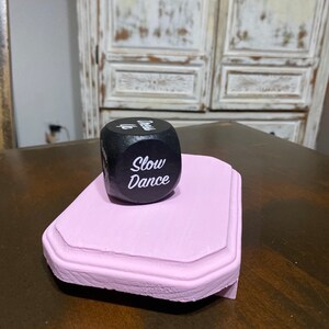 May include: A black wooden dice with white lettering that reads "Slow Dance" on a pink wooden base.