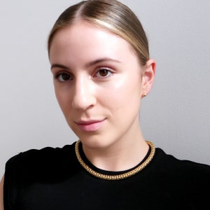 Op de afbeelding: Een vrouw draagt een zwart topje met een gouden ketting.