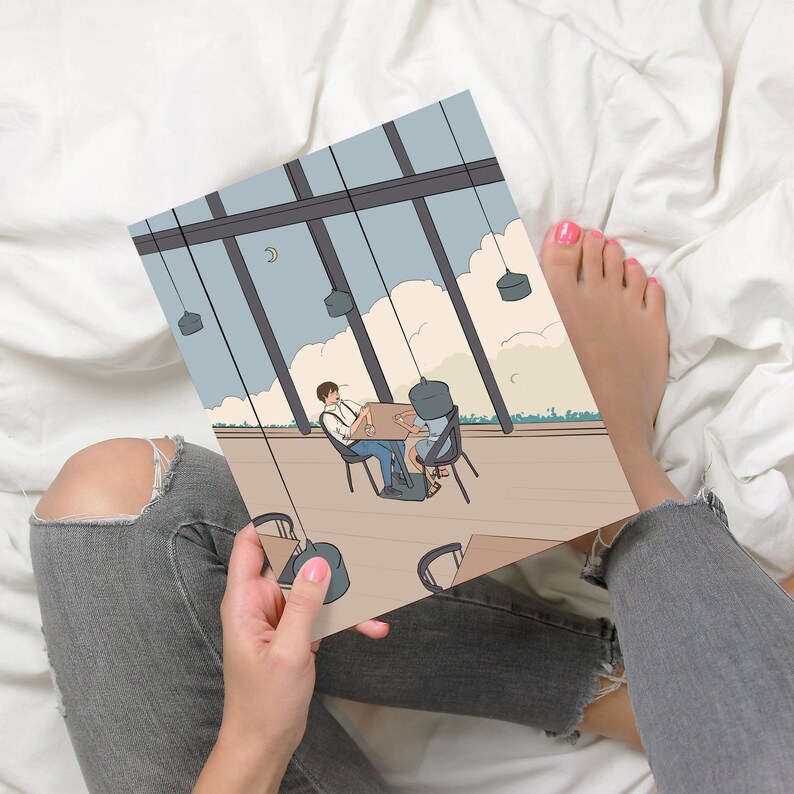 May include: A person is holding a drawing of a couple sitting at a table in a cafe. The cafe has large windows and a view of the sky. The drawing is in a cartoon style.
