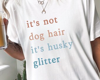 May include: White t-shirt with the text "it's not dog hair it's husky glitter" in different shades of blue, orange, and brown.