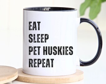 May include: White ceramic coffee mug with a black rim and handle. The mug has black text that reads "Eat Sleep Pet Huskies Repeat".