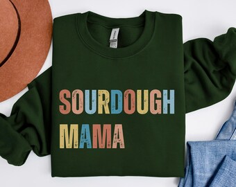 May include: A dark green sweatshirt with the text "SOURDOUGH MAMA" in colorful retro-style lettering.
