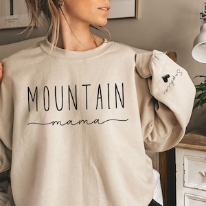 May include: A beige sweatshirt with the text "MOUNTAIN mama" printed on the front and a small heart with the text "Sophia" on the sleeve.