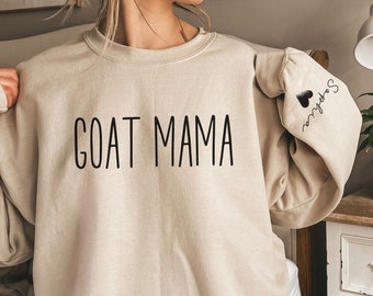 Puede incluir: Una sudadera de color arena con el texto "GOAT MAMA" impreso en la parte delantera y "So fly" con un corazón en la manga.