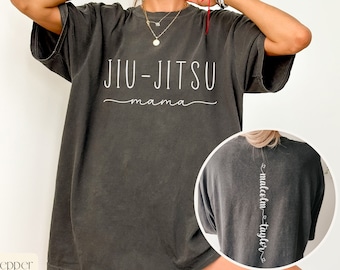 May include: A dark gray oversized t-shirt with the text "JIU-JITSU mama" printed on the front. The back of the shirt has the text "malcolm - taylor" printed vertically down the center.