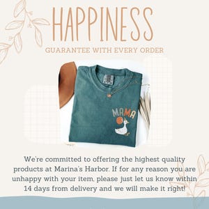 Puede incluir: Una camiseta de color verde azulado con la palabra "MAMA" en letras naranjas y blancas, un dibujo de un ganso y un collar dorado. La imagen tambi&eacute;n incluye el texto "HAPPINESS GUARANTEE WITH EVERY ORDER."