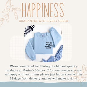Puede incluir: Una sudadera azul claro con el texto "maybe wine is addicted to me". La imagen tambi&eacute;n incluye un par de vaqueros azules y un art&iacute;culo a rayas blancas y negras. La palabra "HAPPINESS" est&aacute; en la parte superior de la imagen.